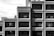 Concrete brutalist building with a uniform grid of rectangular windows. The structure features an industrial and geometric design, casting strong shadows due to the angle of sunlight. The visible portion of the building is composed of repetitive patterns and forms.