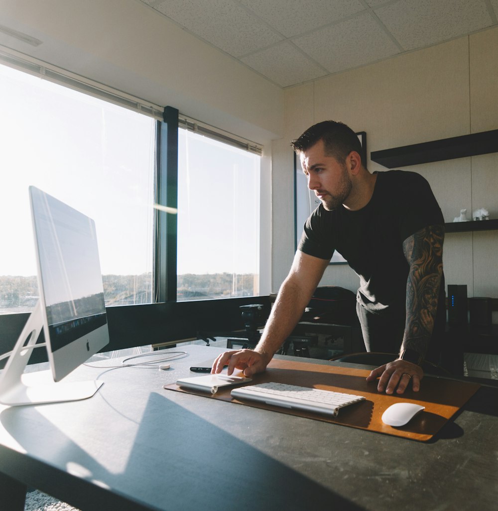 homme en chemise noire debout et utilisant un ordinateur à l’intérieur du bureau pendant la journée