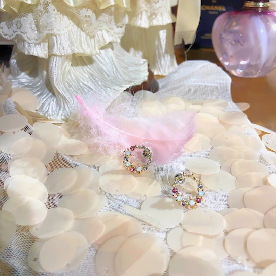 Soft blush pink floral arrangement beside elegant gold jewelry on ivory background