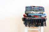 A neatly folded stack of multicolored eastern fabrics arranged on a cozy woven rug.