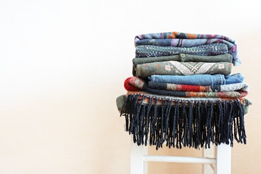 A vibrant stack of colorful, eco-friendly clothing and accessories displayed on a rustic wooden table.
