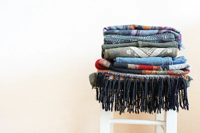 A neatly folded stack of multicolored eastern fabrics arranged on a cozy woven rug.