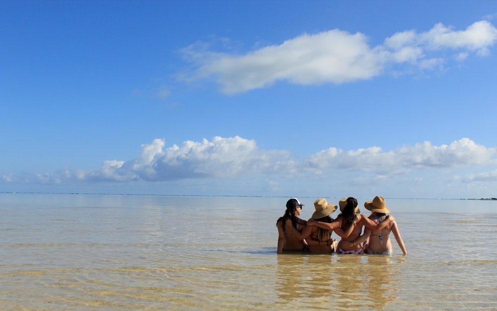 four women sitting on body of water during daytime