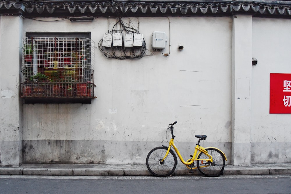 yellow bicycle parked beside white concrete wall