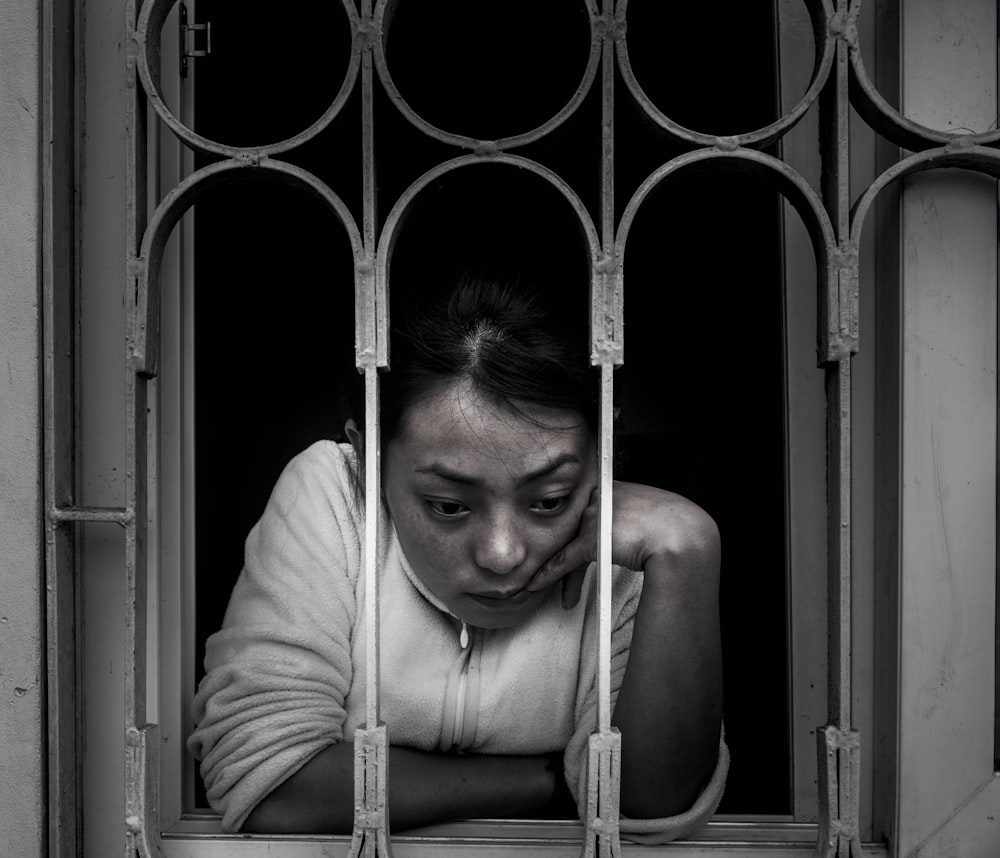 grayscale photography of woman looking out a window