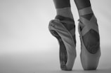 Close-up of a pair of ballet pointe shoes worn by a dancer, showcasing the delicate ribbons wrapped around the ankles and the worn tips of the shoes that indicate frequent use.