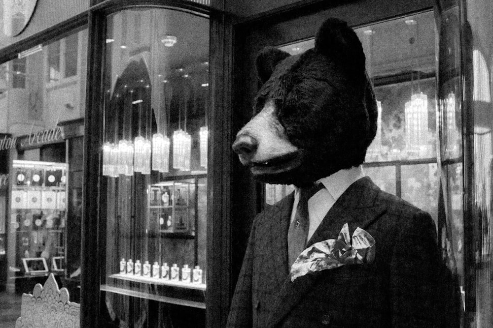 Photographie en niveaux de gris d’une personne avec un masque de loup debout près d’un magasin de vitrine en verre