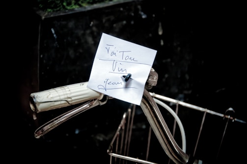 A close-up of a vintage bicycle handlebar with a handwritten note attached.