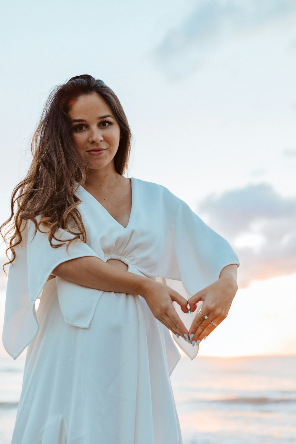 woman wearing white dress making heart hand sign