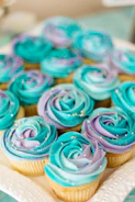 An assortment of colorful cupcakes with swirls of frosting and sprinkles on a white platter.