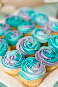 Close-up of a tray filled with assorted colorful cupcakes topped with swirls of pastel icing.