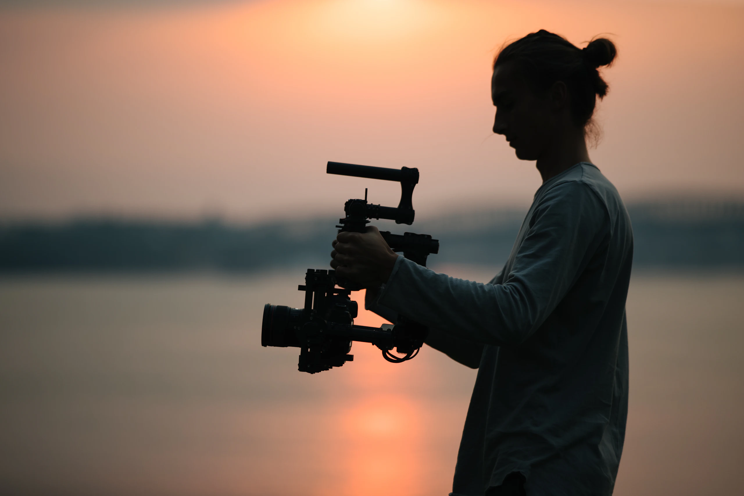 A filmmaker holds a camera rig against a glowing sunset
