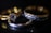 A close-up view of three rings placed on a dark surface. One of the rings features a large, sparkling gemstone, while the others display intricate metal patterns. The lighting creates a dramatic and elegant effect, highlighting the metallic shine and gemstone clarity.