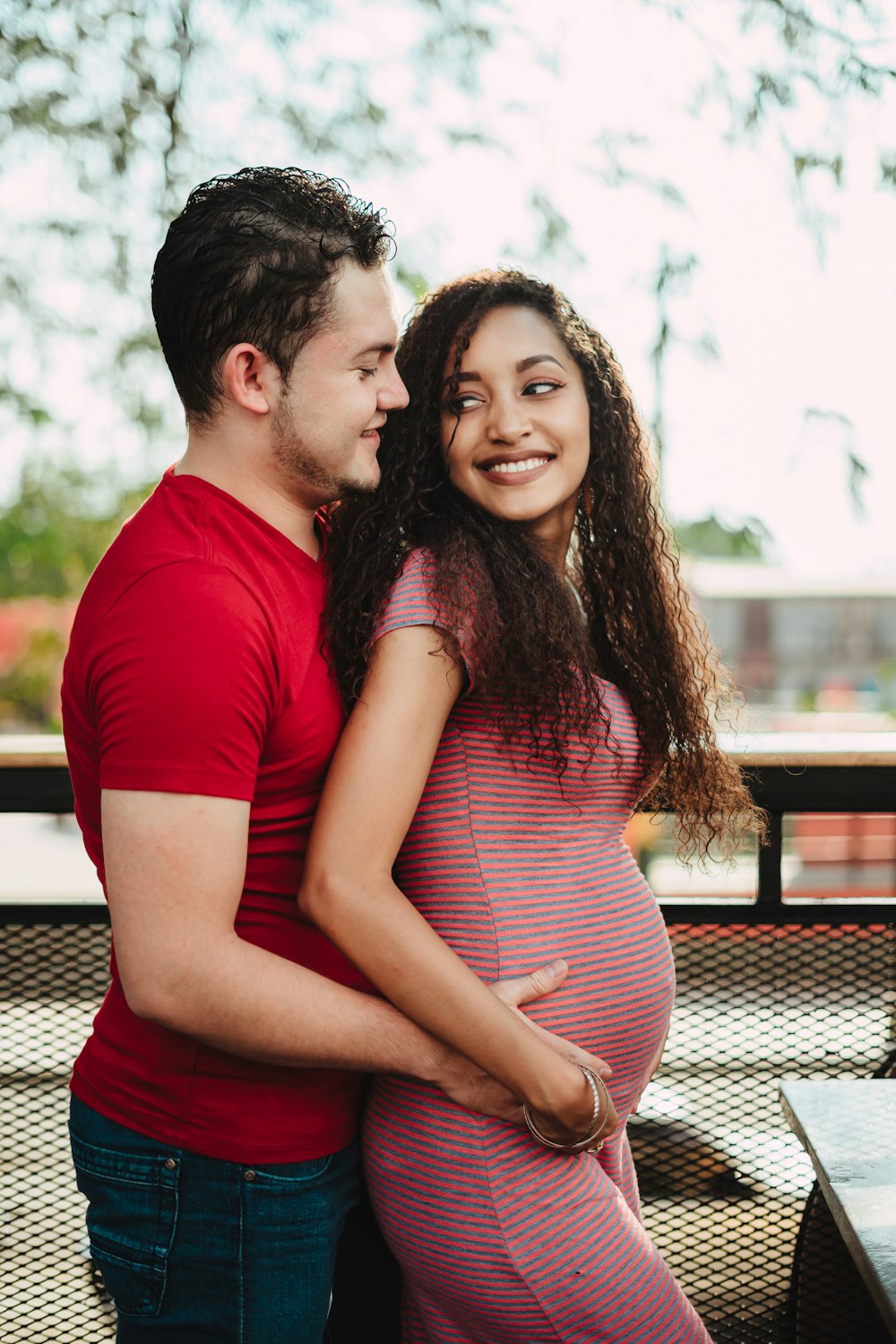 man in rd t-shirt holding pregnant woman's belly