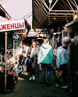 Model walking through a bustling street market wearing a colorful, layered jacket and matching sneakers.