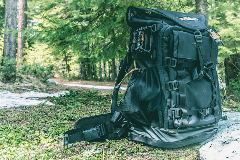 A sleek black and rose gold hiking backpack resting on a sunlit forest trail.