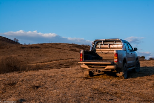 A rugged pickup truck parked beside a winding dirt trail under a vast blue sky.