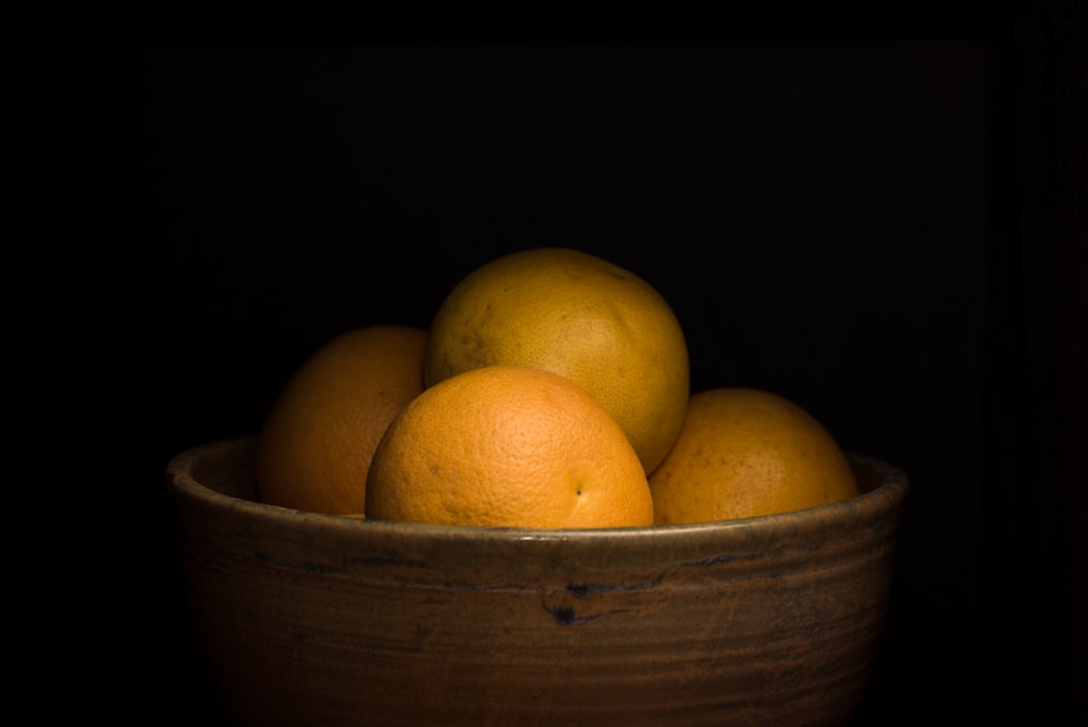 cuatro frutos naranjas en una olla marrón