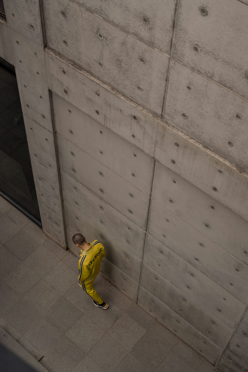 Homme en veste de survêtement et pantalon jaune marchant le long du mur de béton gris