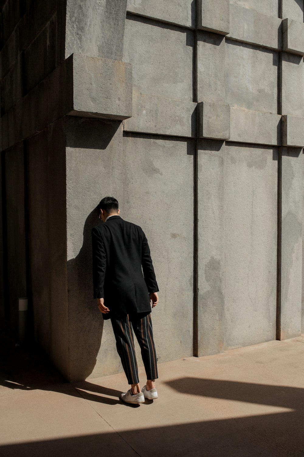 man in black suit banging his head on wall