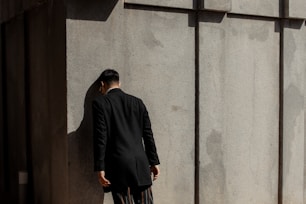 man in black suit banging his head on wall