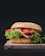 A fresh, gourmet sandwich is placed on a wooden board. The sandwich consists of a sesame seed bun filled with leafy green lettuce, slices of tomato, and layers of roast beef. The vibrant colors of the ingredients stand out against a dark background.