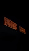 Two neon signs with orange outlines displaying the words 'DRUGS' and 'LIQUOR' against a dark background.