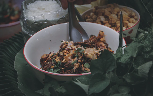 A rustic bowl filled with colorful millet chivda surrounded by fresh green leaves.