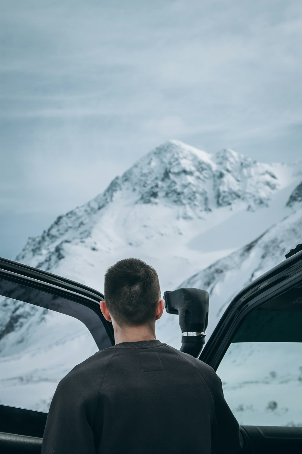 눈 덮인 산을 마주보고 있는 차량의 열린 문 옆에 서 있는 남자