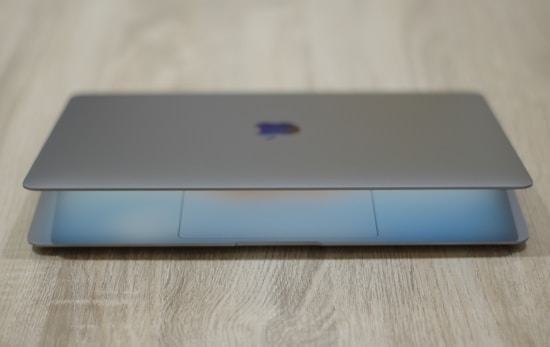 A sleek, modern laptop partially open on a wooden surface. The lid is slightly ajar, revealing the glow of the screen. The device has a metallic finish and a minimalist design.