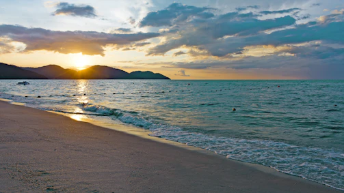 Golden sandy beach with gentle waves and a colorful sunset sky.