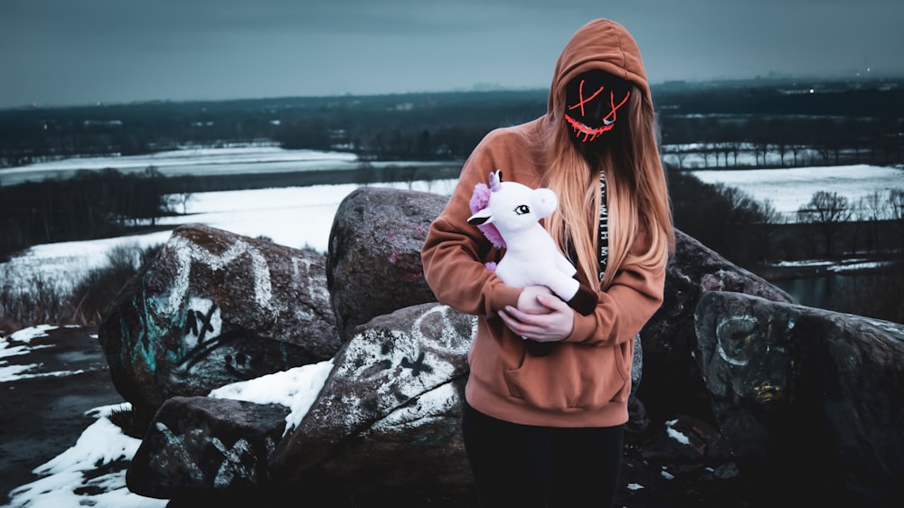 woman standing on boulder holding plush toy