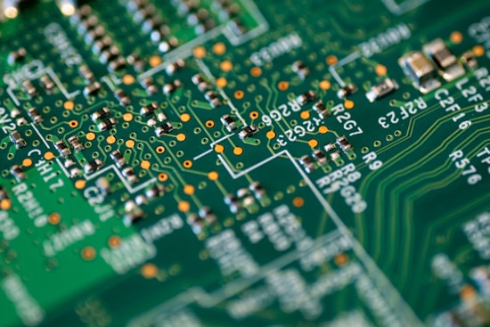 A close-up of a green circuit board featuring intricate pathways, soldered connections, and electronic components such as resistors and capacitors. The board is densely packed with various small parts connected by fine lines.