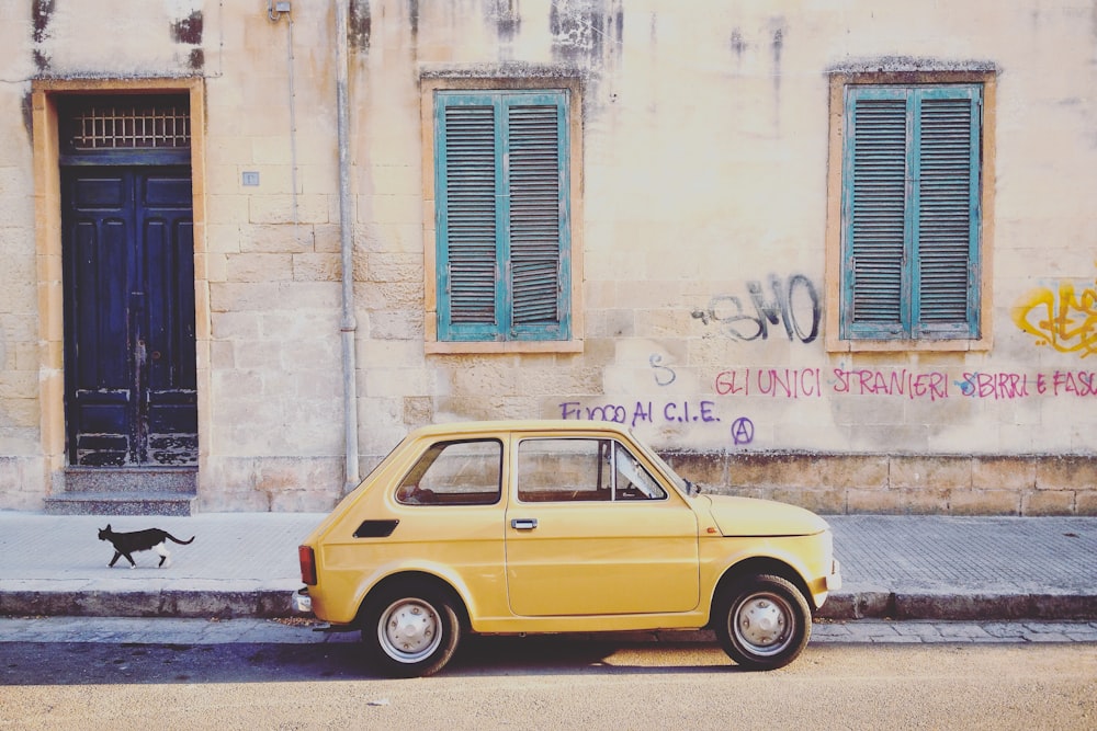 yellow hatchback parked near brown building