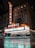 A nighttime street scene featuring a large illuminated marquee sign for the Chicago Theater. The sign reads 'Chicago' vertically and horizontally, adorned with colorful lights. The building has an ornate architectural design. The wet pavement in the foreground reflects the neon lights, adding a moody effect to the scene.