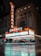 A nighttime street scene featuring a large illuminated marquee sign for the Chicago Theater. The sign reads 'Chicago' vertically and horizontally, adorned with colorful lights. The building has an ornate architectural design. The wet pavement in the foreground reflects the neon lights, adding a moody effect to the scene.
