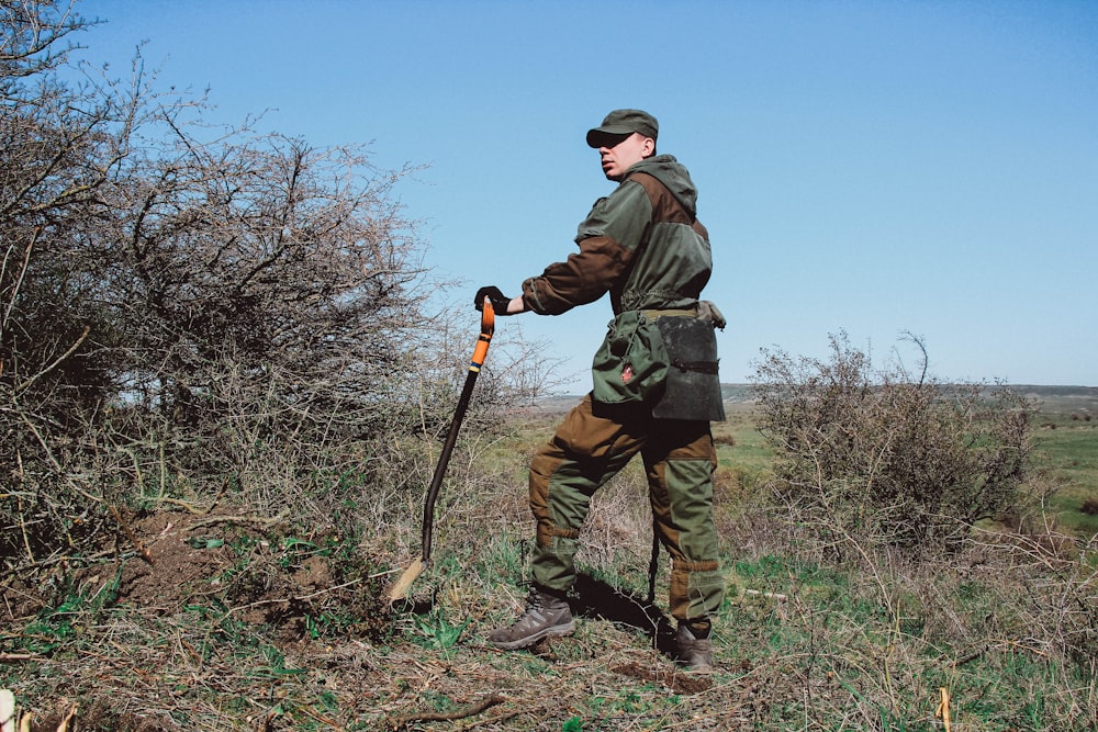 man standing while holding shovel outdoors during daytime