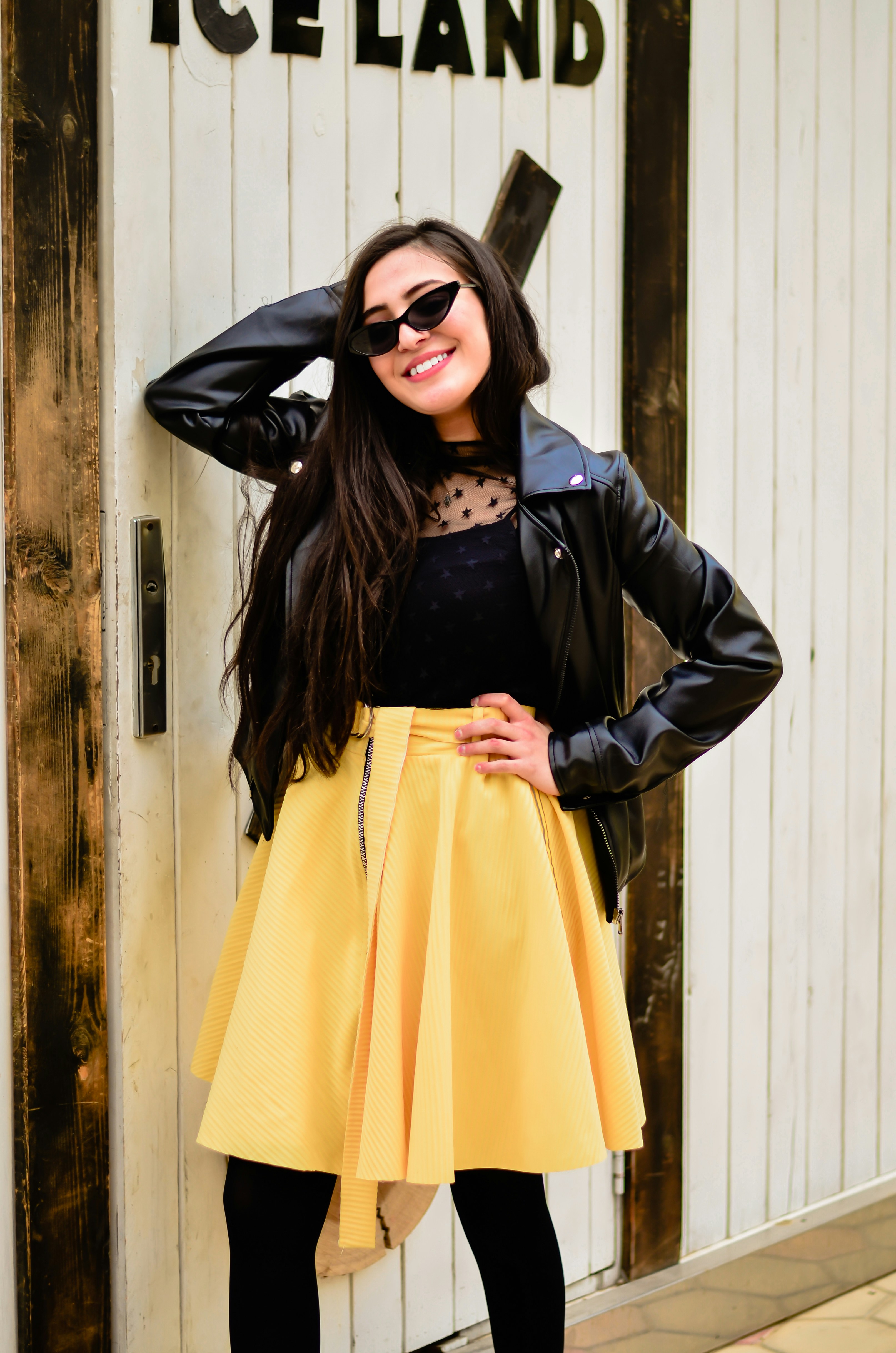 Foto mujer con chaqueta negra y falda amarilla al lado de la puerta – Imagen Vestir gratis