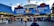 A bustling seafood market scene with a blue and red-themed storefront. The market features prominent signage advertising fresh fish, shrimp, lobster, jumbo crabs, and cooked crabs. Several people are gathered in front of the market, some seemingly in line or browsing.