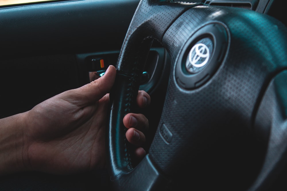 person holding black Toyota vehicle steering wheel