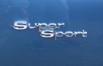 The image features the words 'Super Sport' in shiny, metallic lettering. The background is a smooth, glossy blue surface, likely part of a vehicle.
