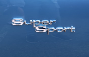 The image features the words 'Super Sport' in shiny, metallic lettering. The background is a smooth, glossy blue surface, likely part of a vehicle.