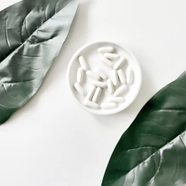 Fresh natural ingredients like herbs and minerals arranged neatly beside white capsules.
