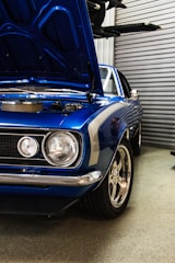 blue muscle car with open hood near roller shutter