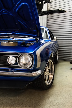 blue muscle car with open hood near roller shutter