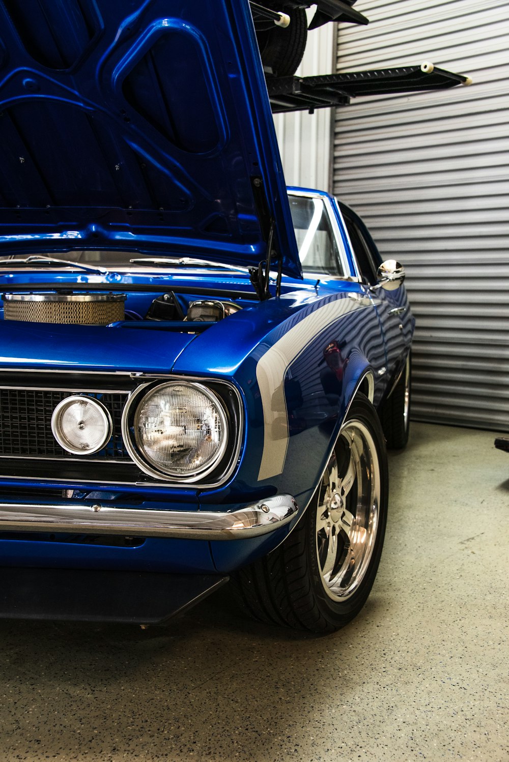 blue muscle car with open hood near roller shutter