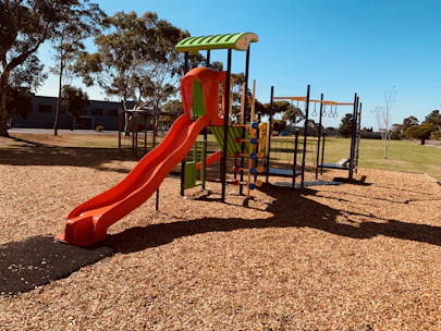 Children playing happily in a spacious, colorful outdoor playground under a clear blue sky.