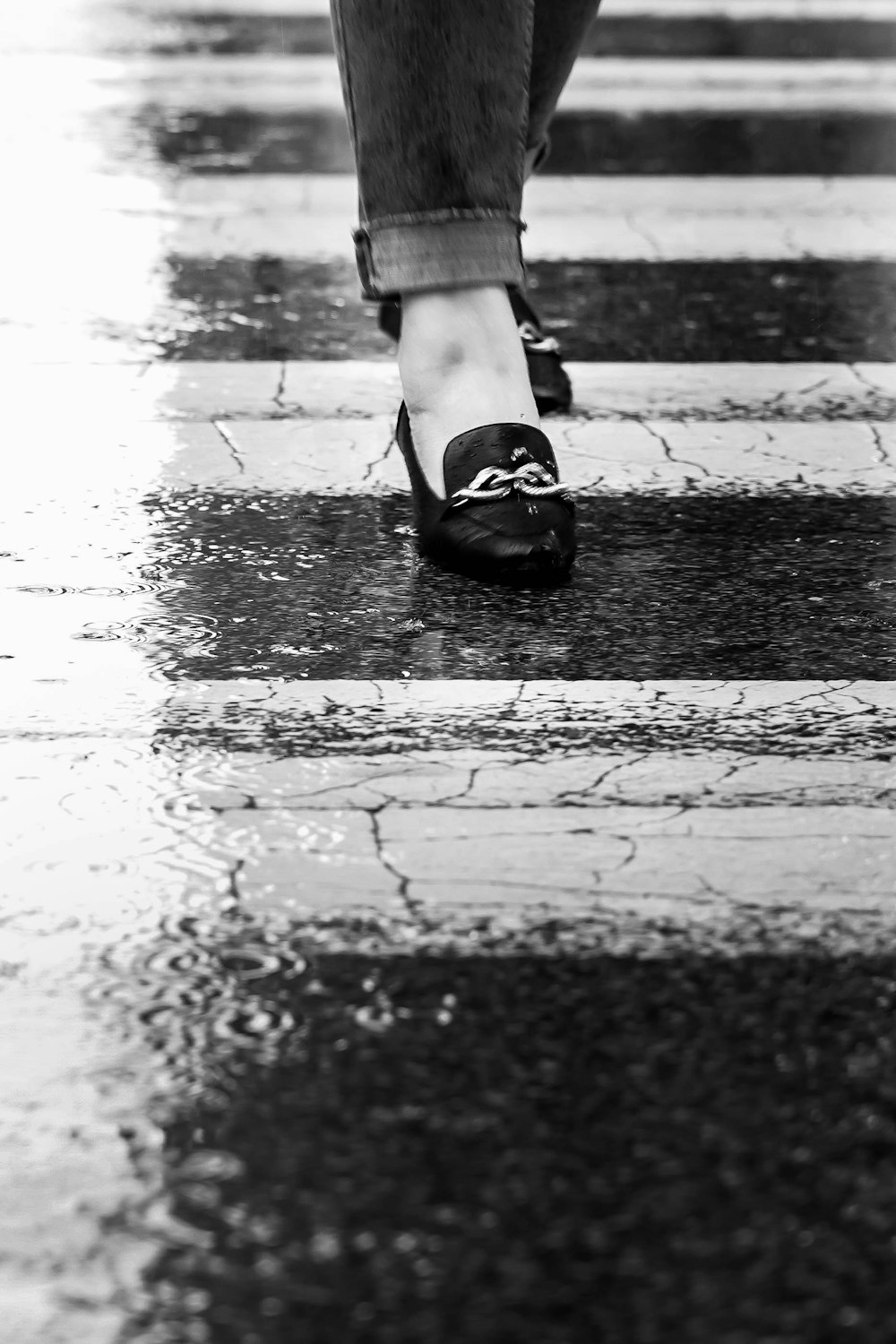 grayscale photography of woman's feet wearing horsebit loafers while walking along pedestrian lane