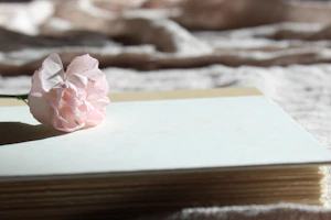 A smiling teenage girl holding a book surrounded by blooming flowers and soft pink tones.