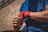 A person wearing a blue shirt is wrapping their hand with red boxing wraps, suggesting preparation for a physical activity, possibly boxing or martial arts. The background appears to be an outdoor space with a building wall.